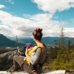A mother sits with her baby overlooking a scenic mountain landscape, enjoying nature's beauty.